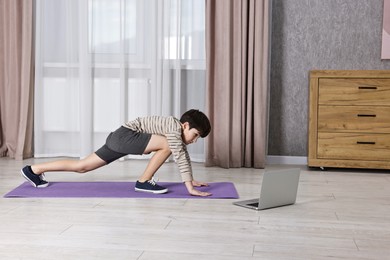 Photo of Little boy exercising near laptop at home. Morning routine