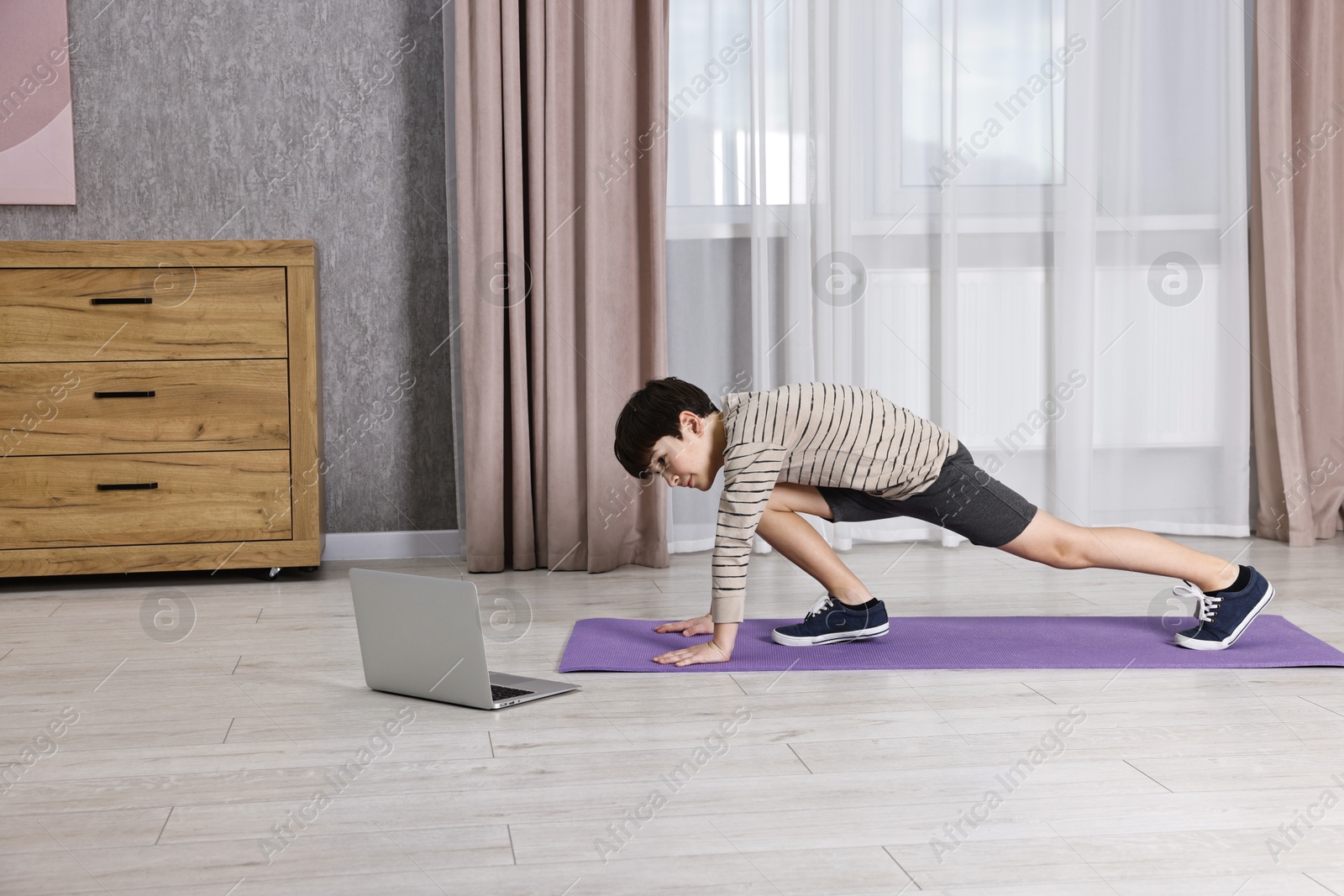 Photo of Little boy exercising near laptop at home. Morning routine