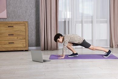 Photo of Little boy exercising near laptop at home. Morning routine