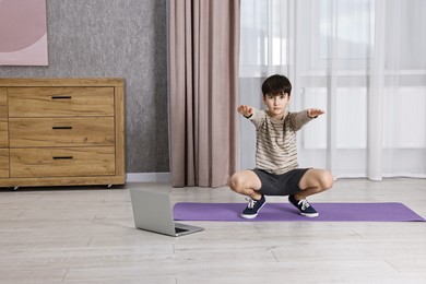 Photo of Little boy exercising near laptop at home. Morning routine