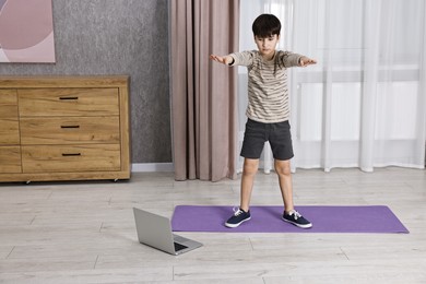 Little boy exercising near laptop at home. Morning routine