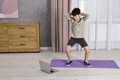 Photo of Little boy exercising near laptop at home. Morning routine