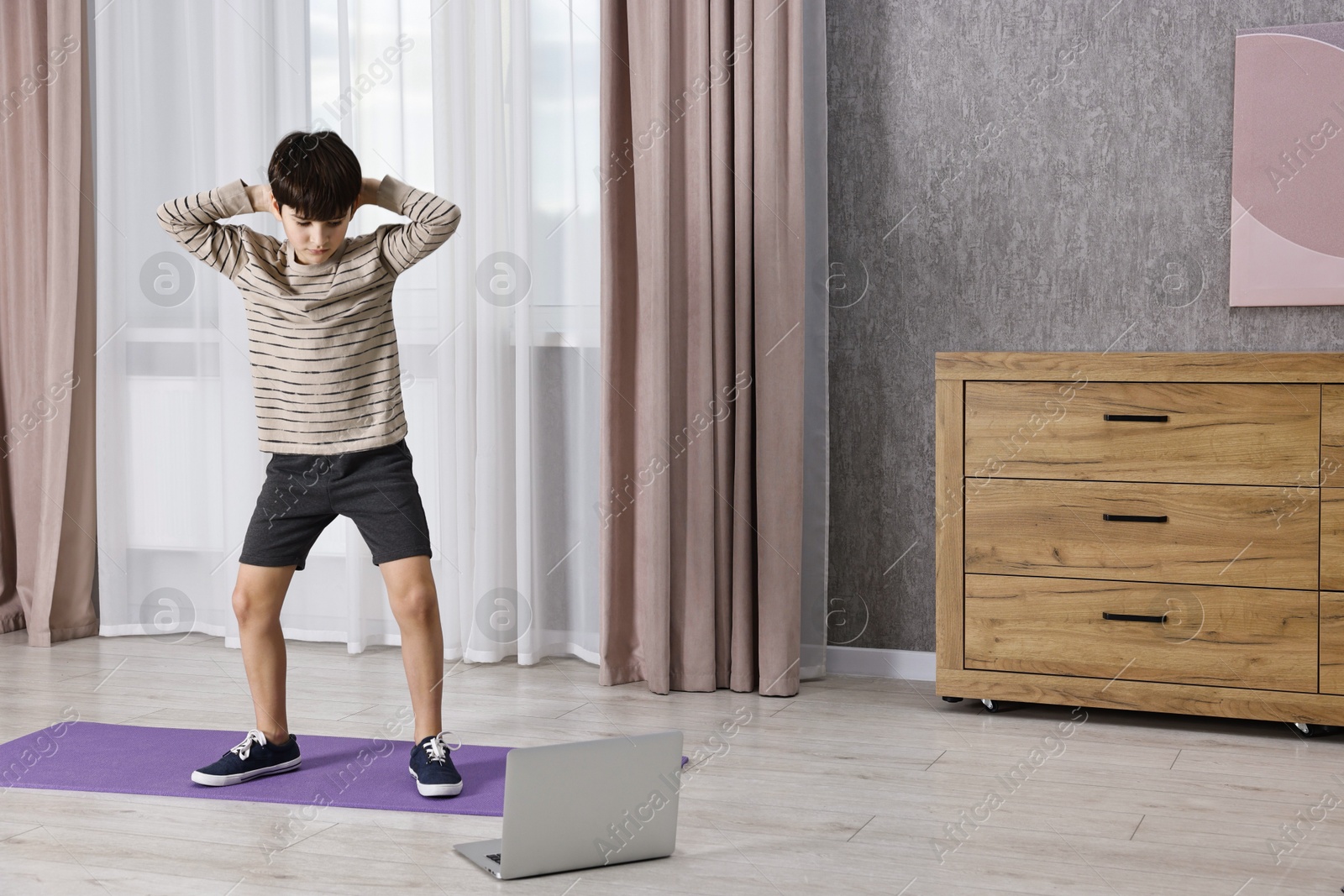 Photo of Little boy exercising near laptop at home. Morning routine