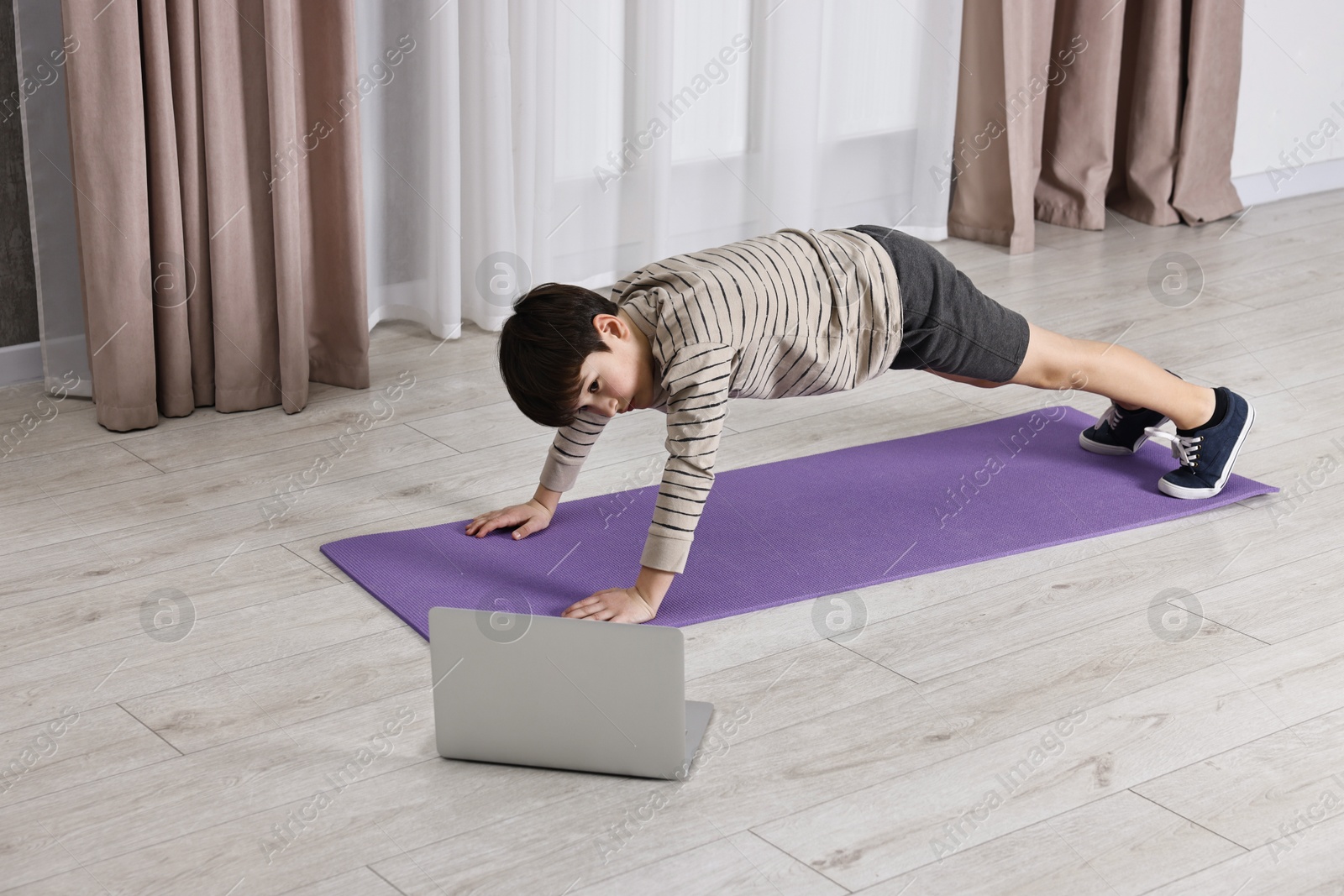 Photo of Little boy exercising near laptop at home. Morning routine