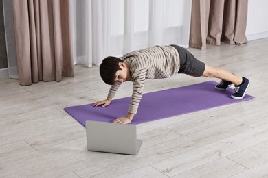 Little boy exercising near laptop at home. Morning routine