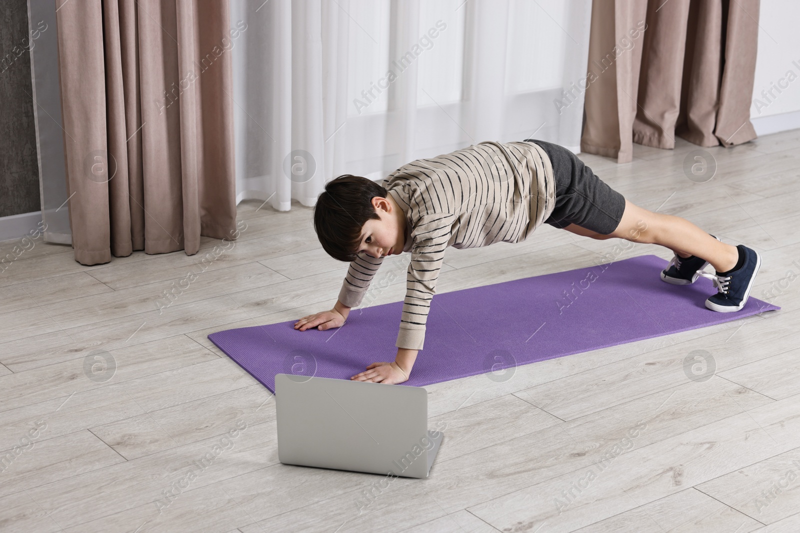 Photo of Little boy exercising near laptop at home. Morning routine