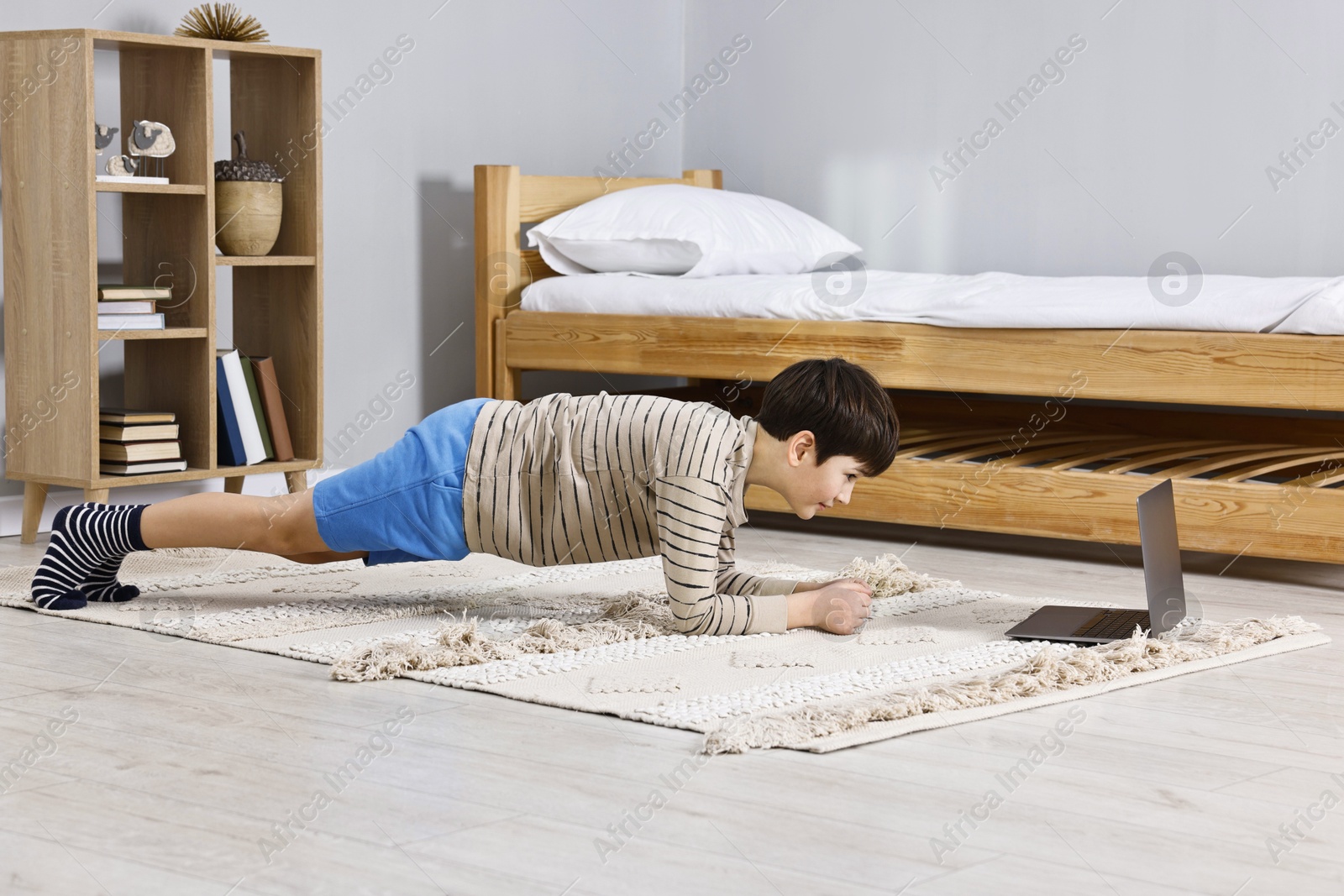 Photo of Little boy doing plank exercise near laptop at home. Morning routine