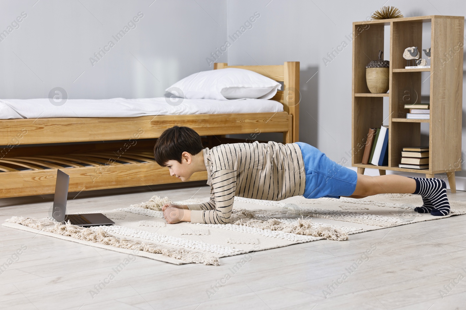 Photo of Little boy doing plank exercise near laptop at home. Morning routine