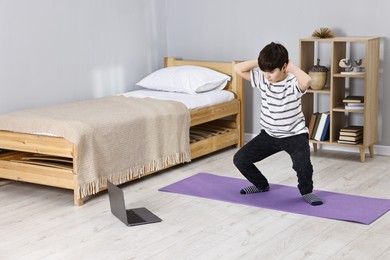 Photo of Little boy exercising near laptop at home. Morning routine