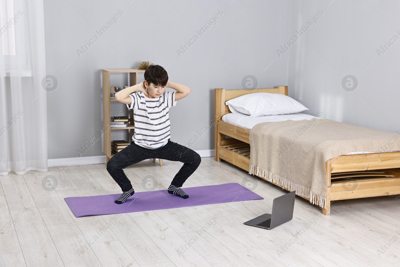 Photo of Little boy exercising near laptop at home. Morning routine