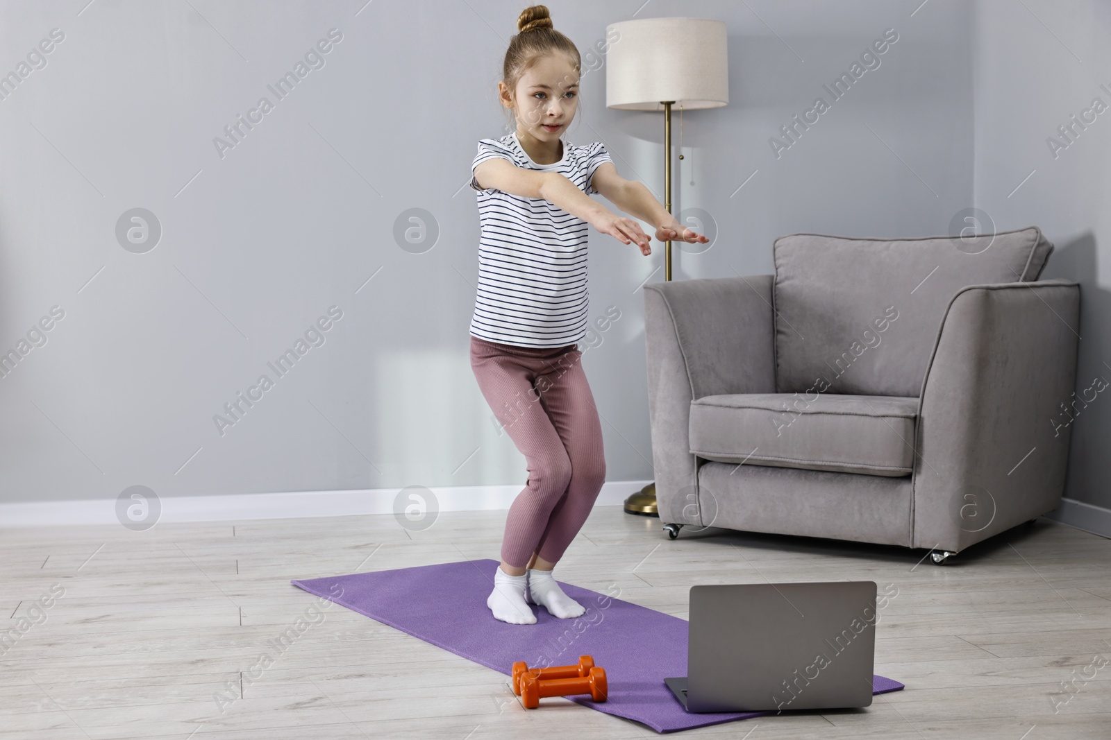 Photo of Little girl exercising near laptop at home, space for text. Morning routine