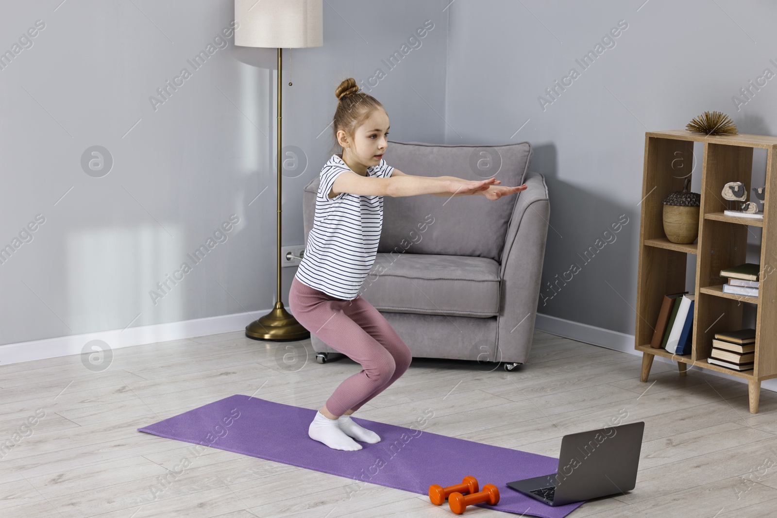 Photo of Little girl exercising near laptop at home. Morning routine