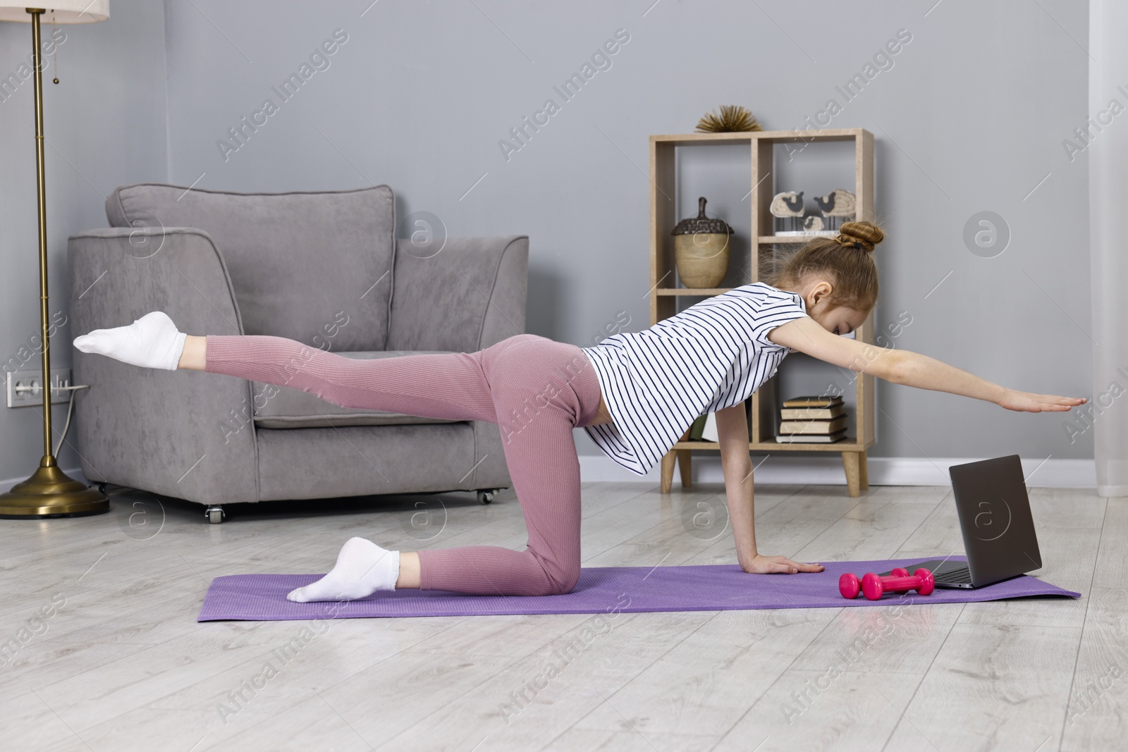 Photo of Little girl exercising near laptop at home. Morning routine