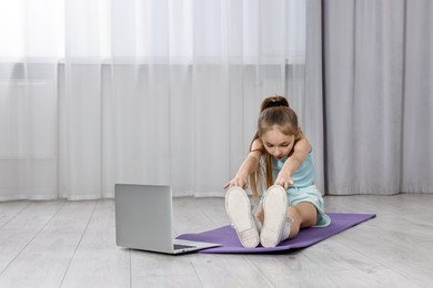 Photo of Little girl exercising near laptop at home, space for text. Morning routine