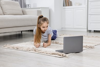 Little girl doing plank exercise near laptop at home. Morning routine