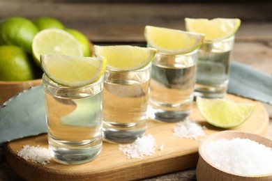 Photo of Tequila shots with lime slices, salt and agave leaves on wooden table, closeup