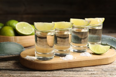 Photo of Tequila shots with lime slices, salt and agave leaves on wooden table