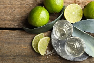 Tequila shots with salt, limes and agave leaves on wooden table, flat lay