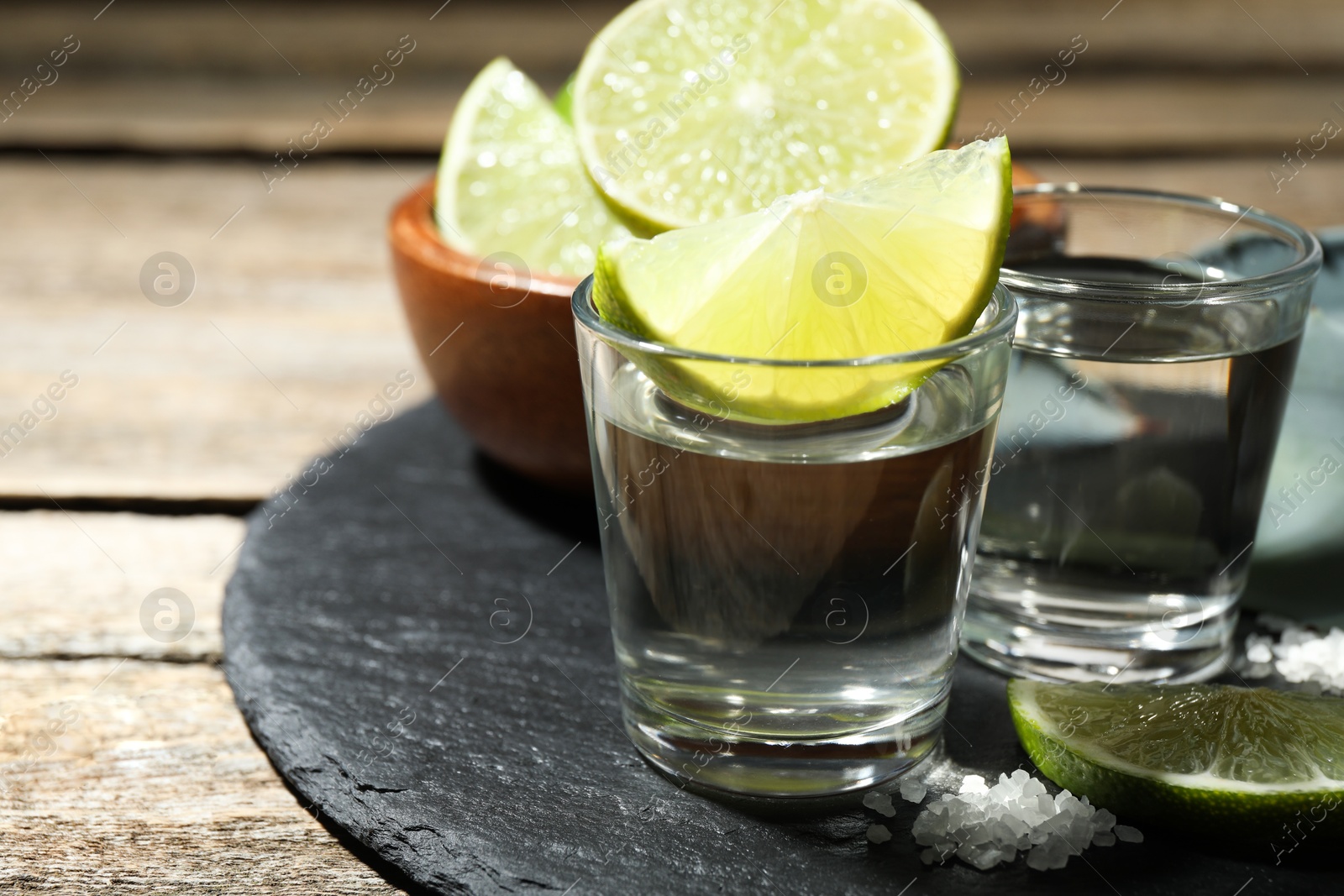 Photo of Tequila shots with lime slices and salt on wooden table, closeup. Space for text