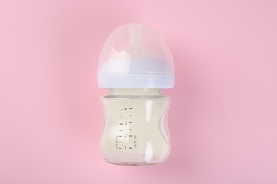 Feeding bottle with milk on pink background, top view