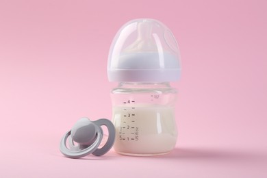 Feeding bottle with milk and pacifier on pink background