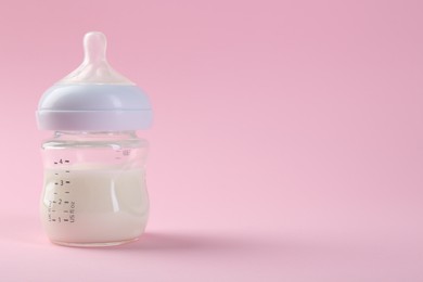 Feeding bottle with milk on pink background, space for text