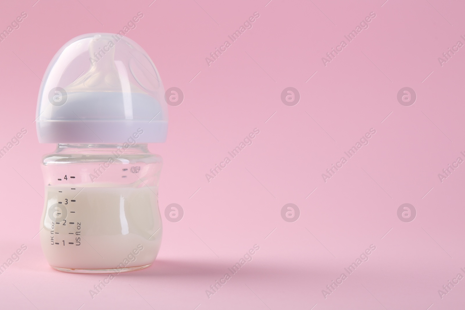 Photo of Feeding bottle with milk on pink background, space for text