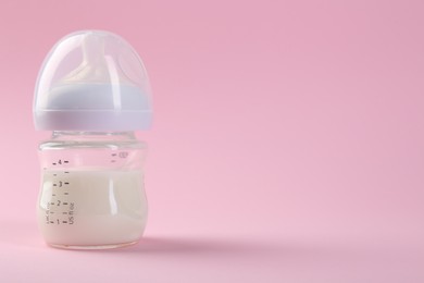 Feeding bottle with milk on pink background, space for text