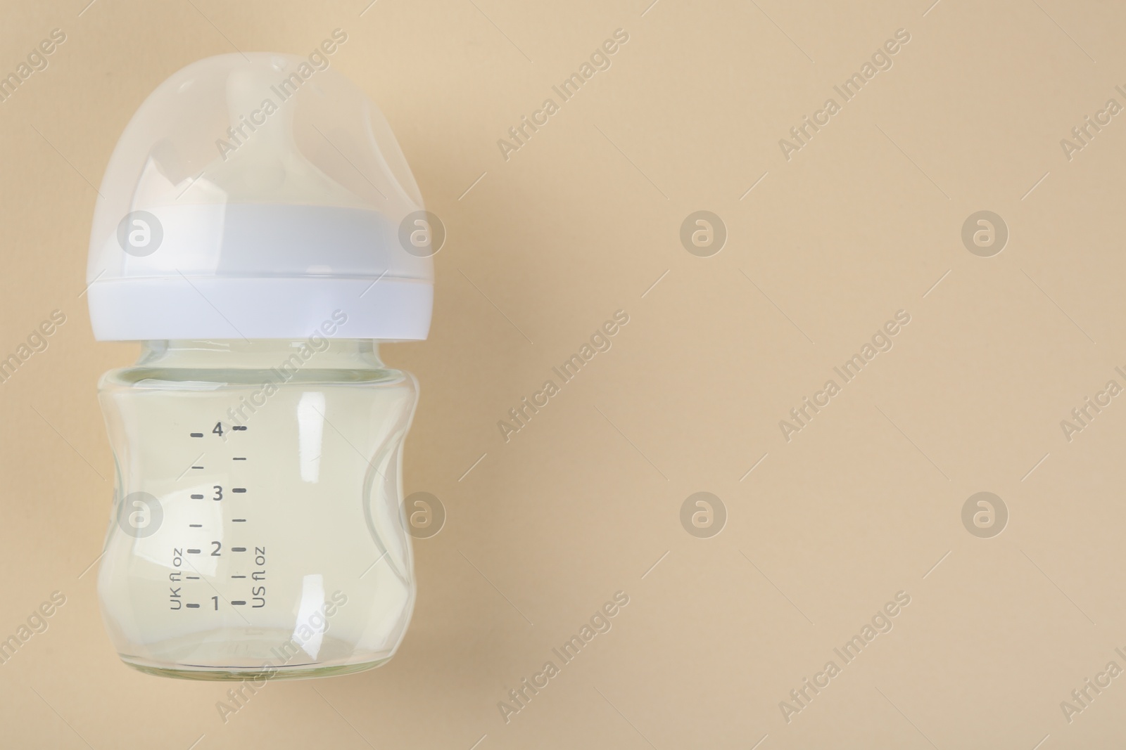 Photo of Feeding bottle with milk on beige background, top view. Space for text