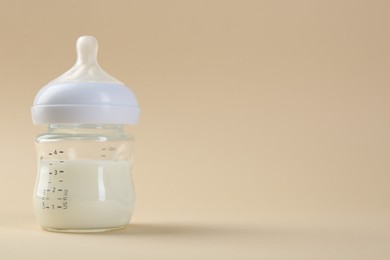 Feeding bottle with milk on beige background, space for text