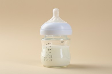 Feeding bottle with milk on beige background