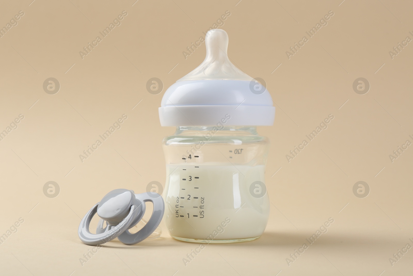 Photo of Feeding bottle with milk and pacifier on beige background