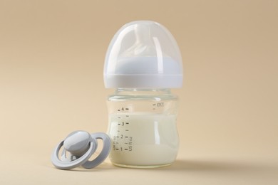 Photo of Feeding bottle with milk and pacifier on beige background