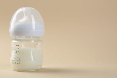 Feeding bottle with milk on beige background, space for text