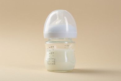 Photo of Feeding bottle with milk on beige background