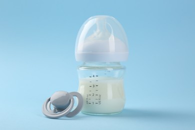 Photo of Feeding bottle with milk and pacifier on light blue background