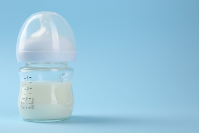 Feeding bottle with milk on light blue background, space for text