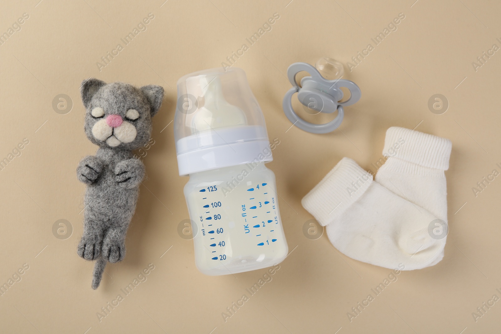 Photo of Feeding bottle with milk, toy, baby socks and pacifier on beige background, flat lay