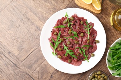 Photo of Fresh beef carpaccio with arugula and capers on wooden table, flat lay. Space for text