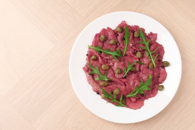 Photo of Fresh beef carpaccio with arugula and capers on wooden table, top view. Space for text