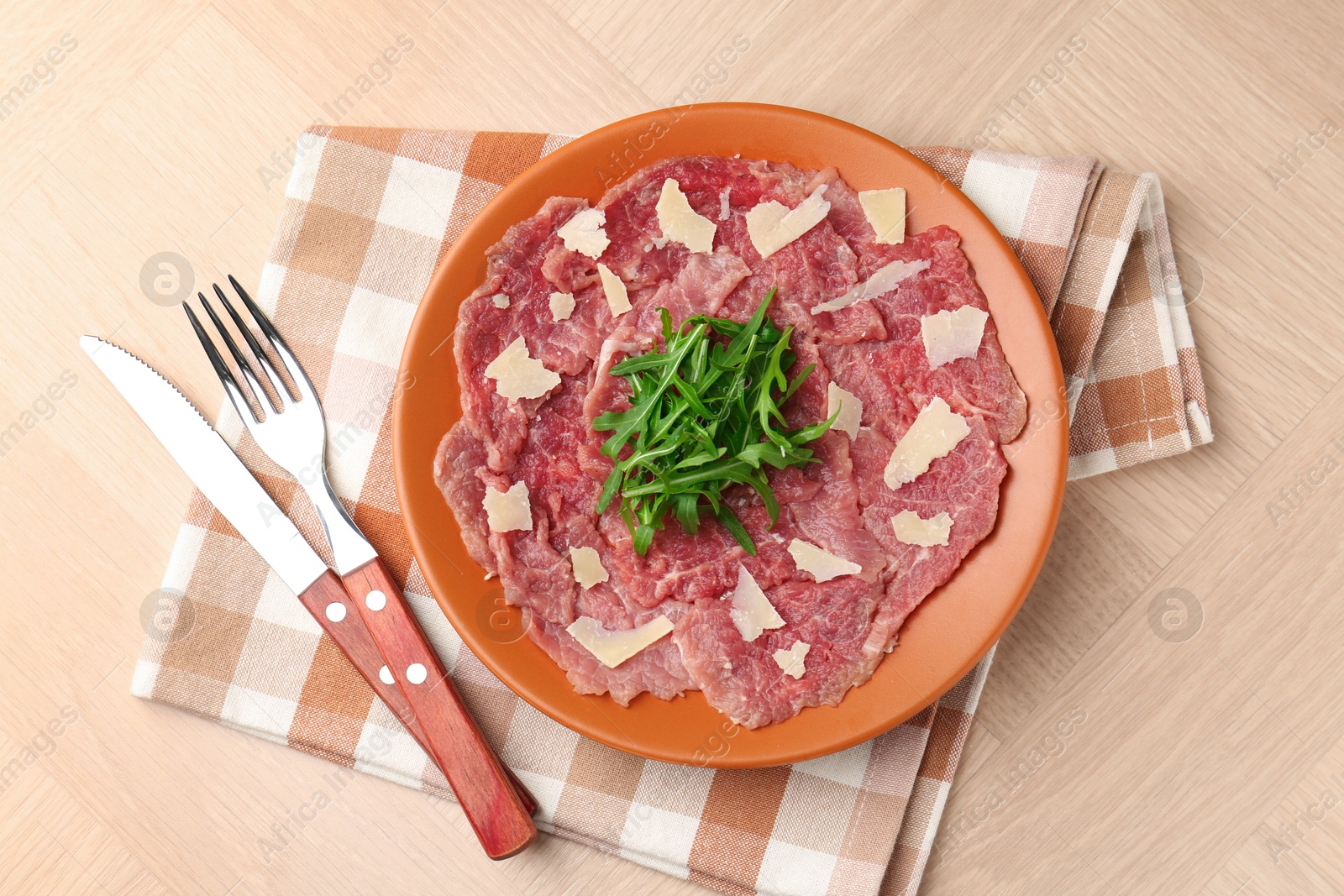 Fresh beef carpaccio with arugula and cheese on wooden table, top view Photo of Fresh beef carpaccio with arugula and cheese on wooden table, top view