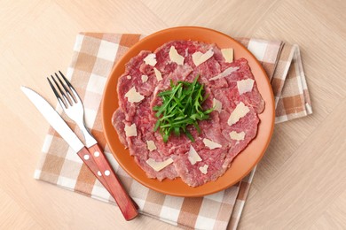 Photo of Fresh beef carpaccio with arugula and cheese on wooden table, top view