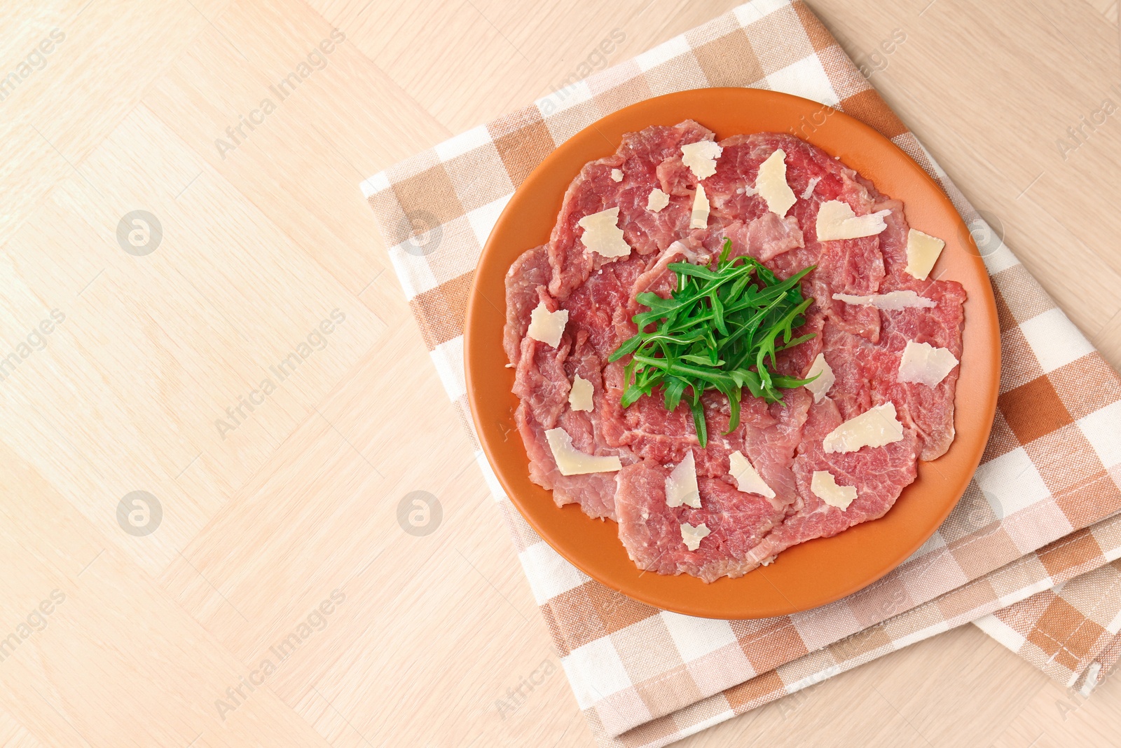 Photo of Fresh beef carpaccio with arugula and cheese on wooden table, top view. Space for text