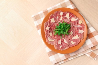 Fresh beef carpaccio with arugula and cheese on wooden table, top view. Space for text