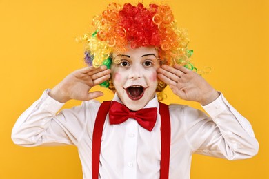 Photo of Emotional little boy dressed like clown on yellow background. Surprise party