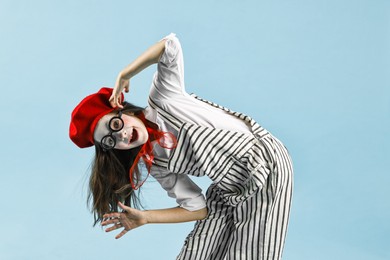 Photo of Happy girl dressed like mime on light blue background. Surprise party