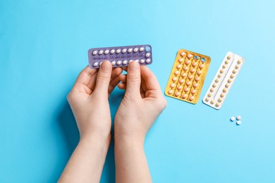 Woman with contraceptive pills on light blue background, closeup