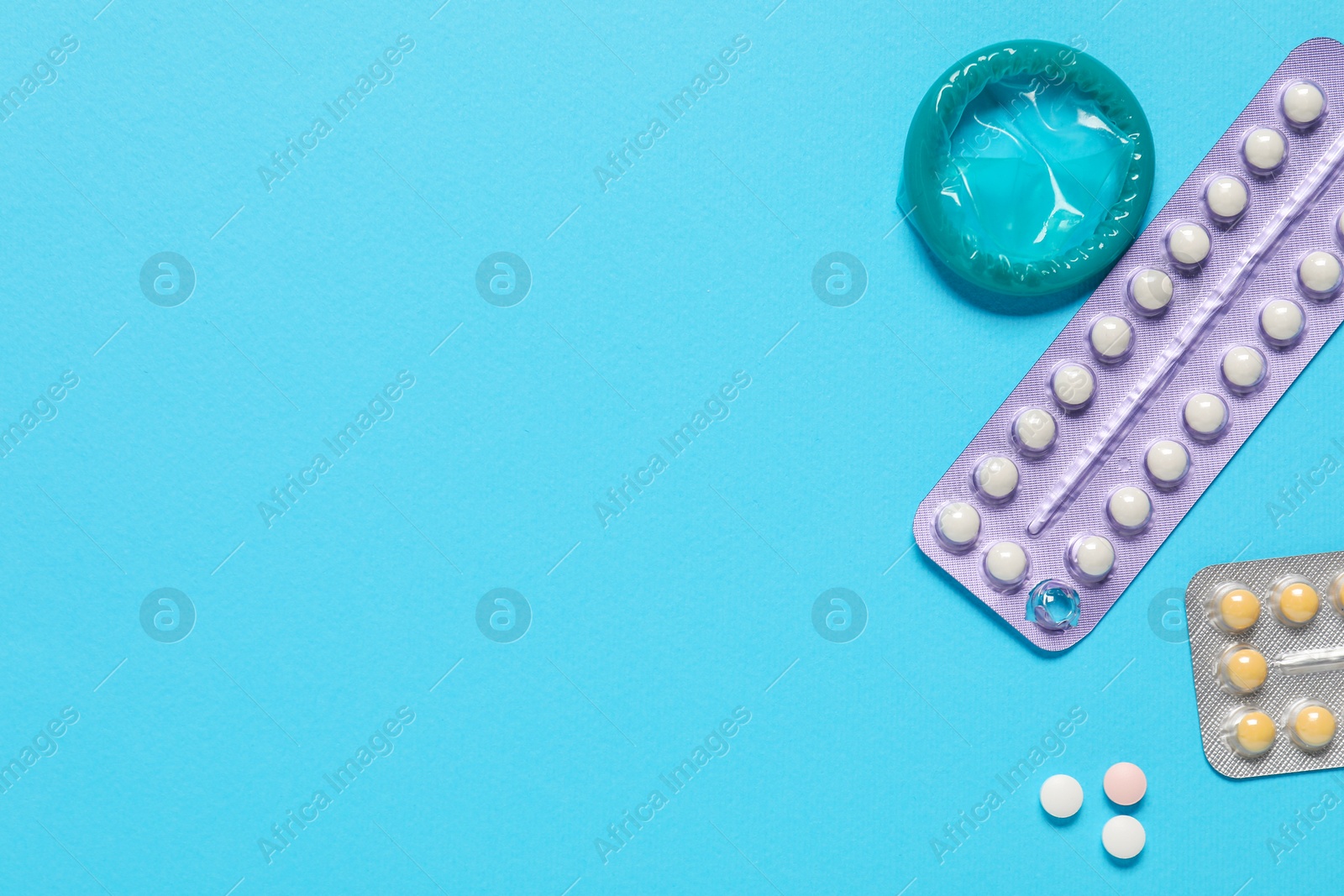 Photo of Contraceptive pills and condom on light blue background, flat lay. Space for text