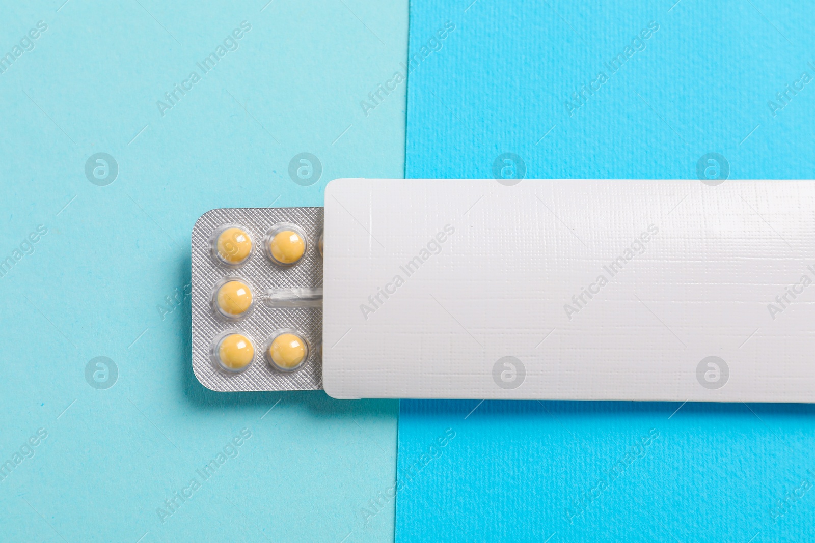 Photo of Blister of contraceptive pills in package on light blue background, top view. Mockup for design