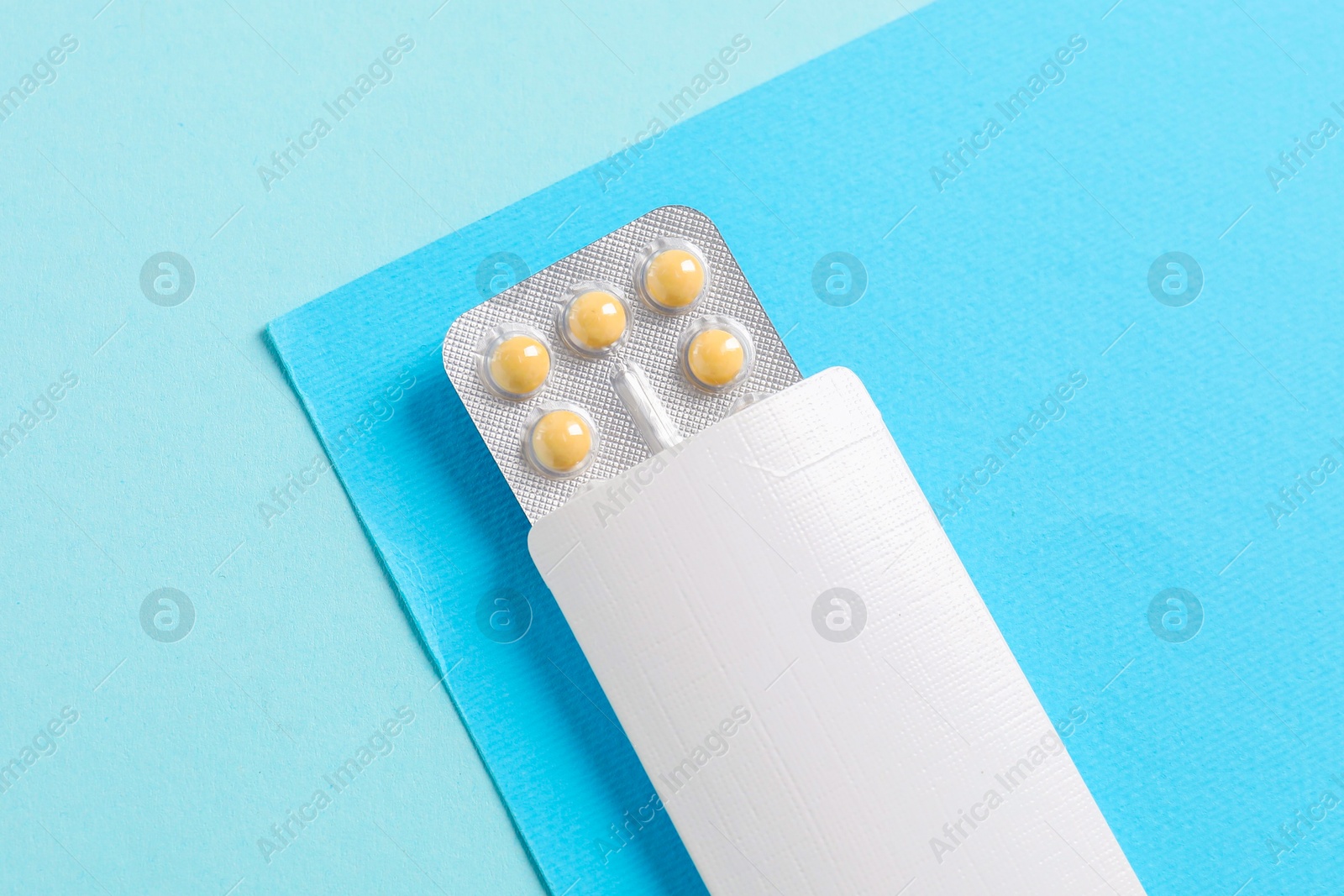 Photo of Blister of contraceptive pills in package on light blue background, top view. Mockup for design